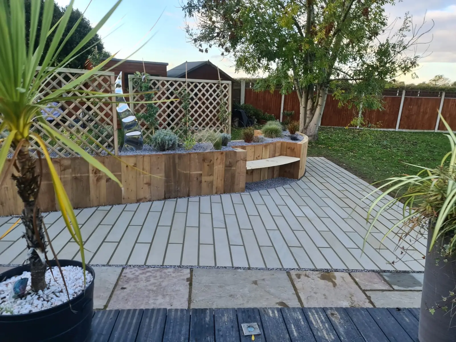 A landscaped garden featuring a patio, seating area, and potted plants under a clear blue sky.