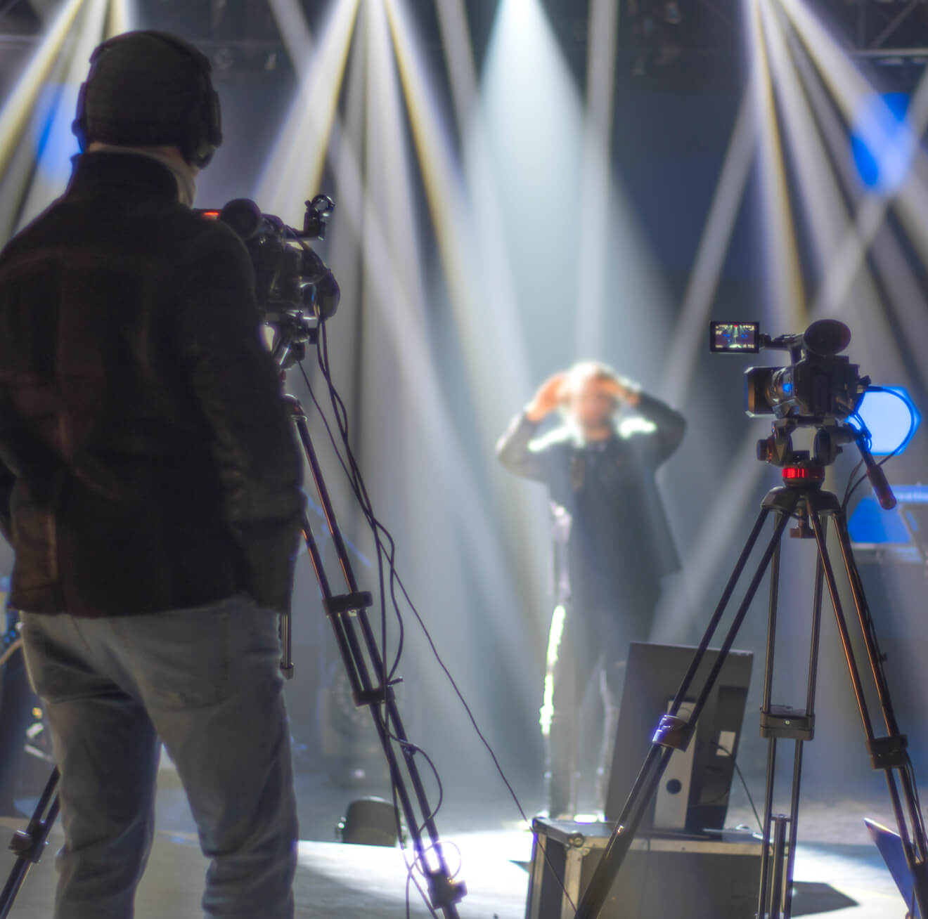 A person stands in front of stage lights, while cameras are positioned to capture the performance.