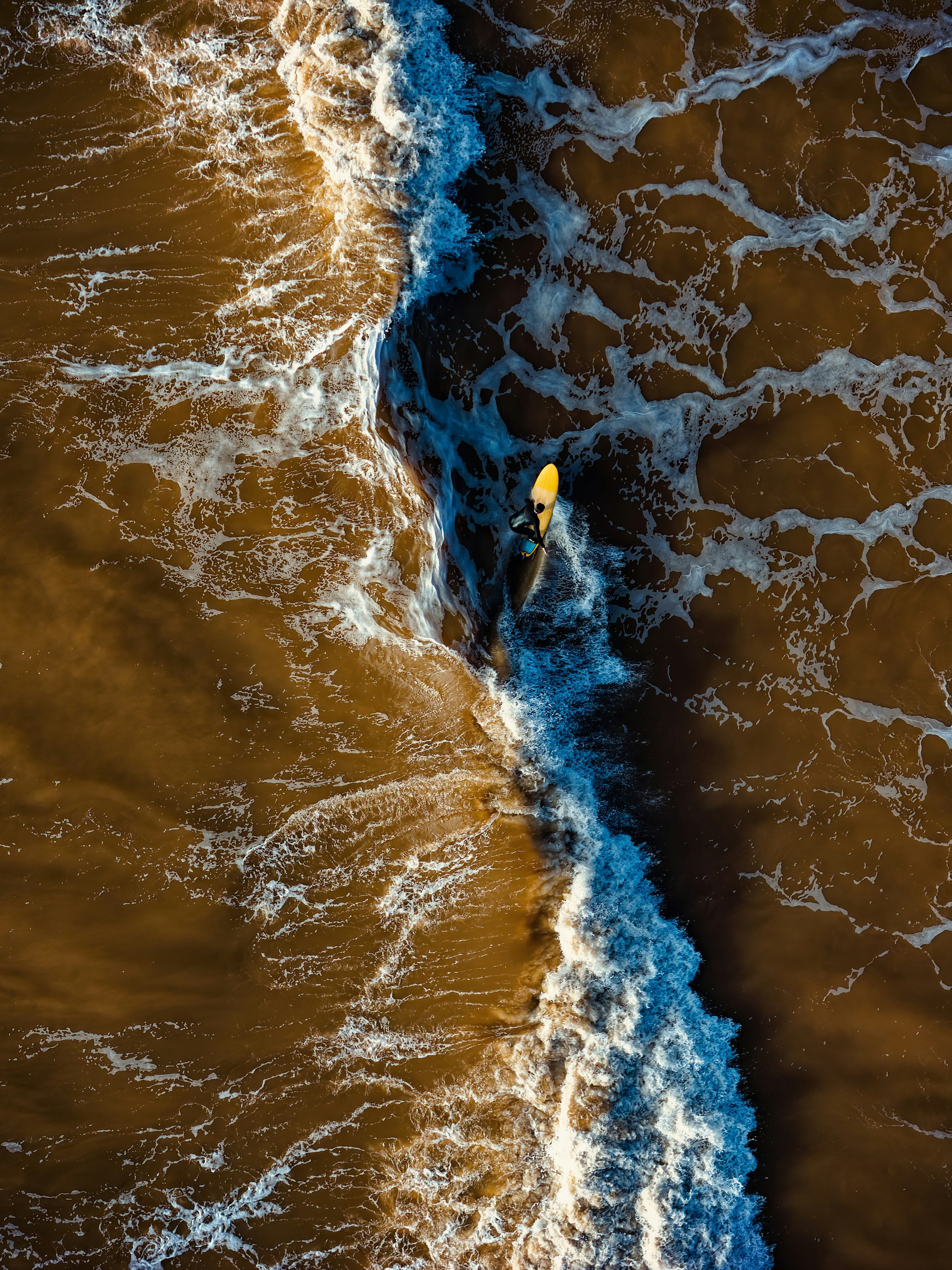 Surfer paddling on a yellow surfboard in brown ocean waves