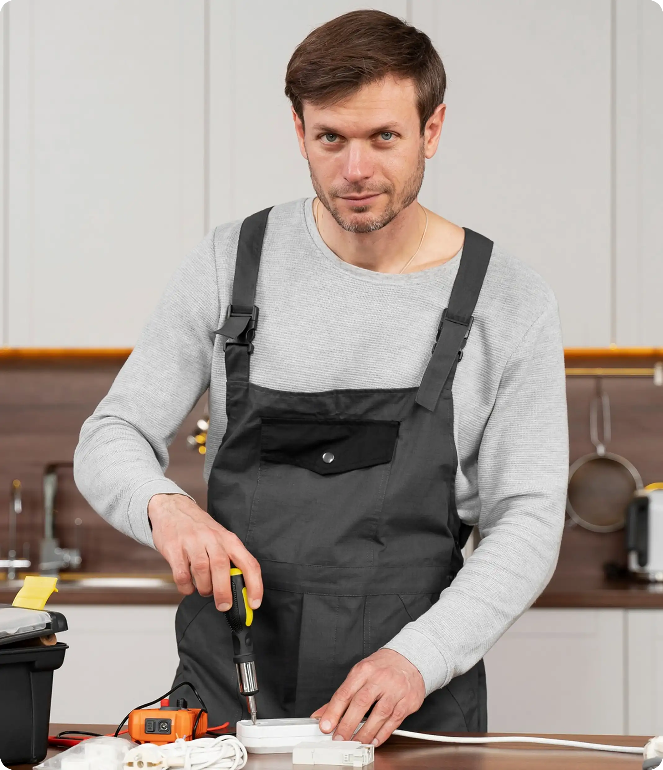 Pipewise technician in grey overalls working with a screwdriver in a kitchen