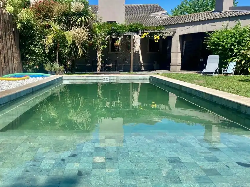 Clásica pileta de jardín exterior terminada con revestimiento de Piedra Bali natural, logrando un tono de agua verde agua cristalino.