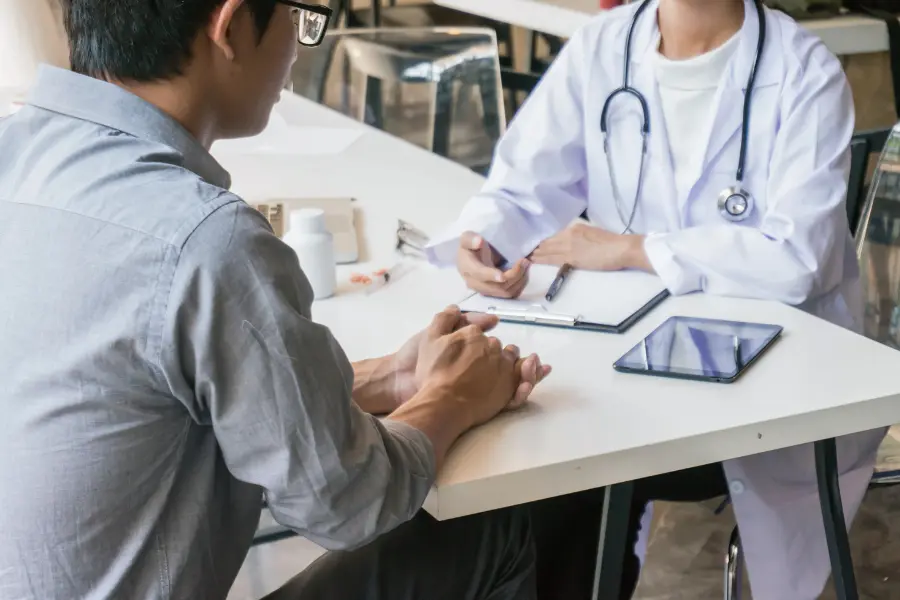 Coding tools for healthcare shown during a doctor-patient consultation with a tablet, clipboard, and medication on the table.