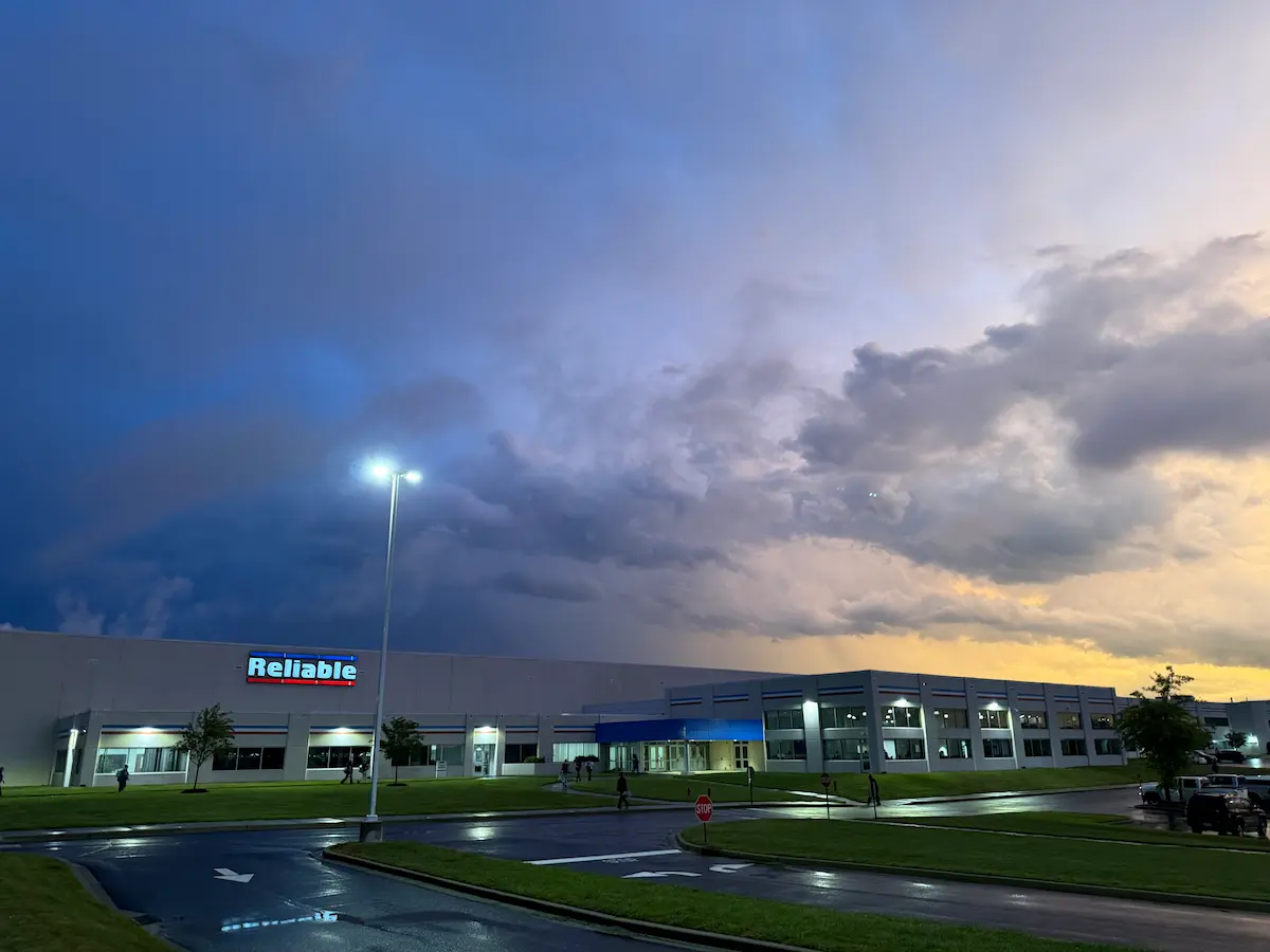 A storm approaches over the Reliable Sprinkler plant, with dark clouds filling the sky while sunlight still shines through behind the building.