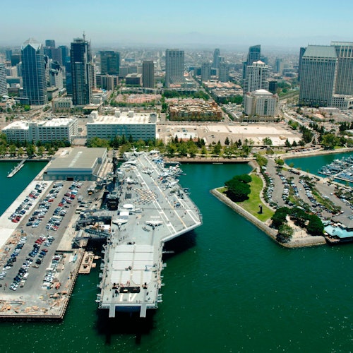 มุมมองจากอากาศของเรือรบที่เทียบท่าที่ท่าเรือ โดยมีภาพเมืองเป็นพื้นหลังและมองเห็นมารีน่าทางด้านขวา