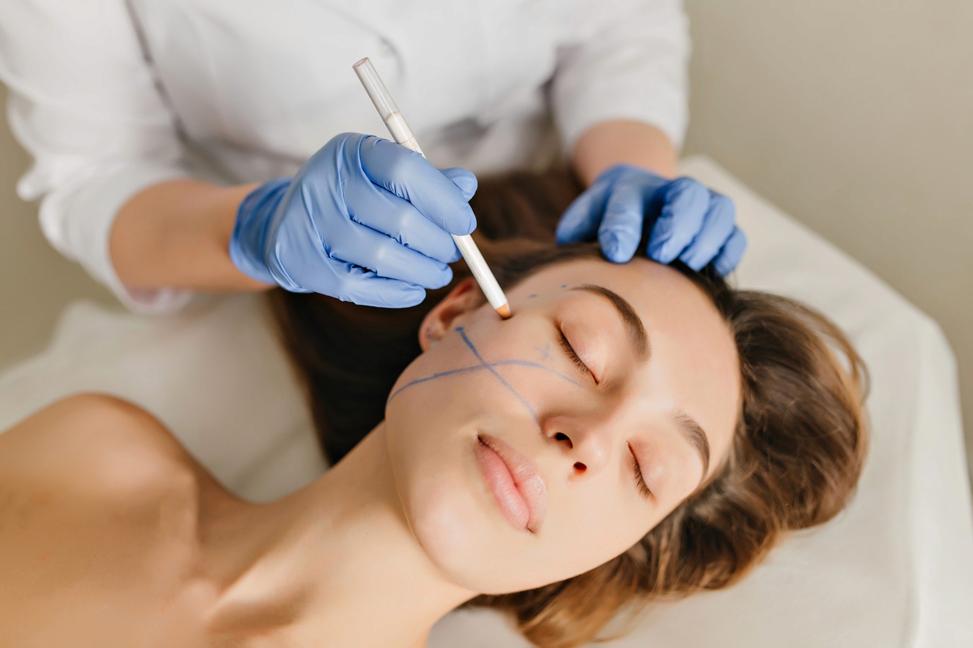 Cosmetologist marking a woman's face with a pencil during a cosmetic procedure, wearing blue gloves