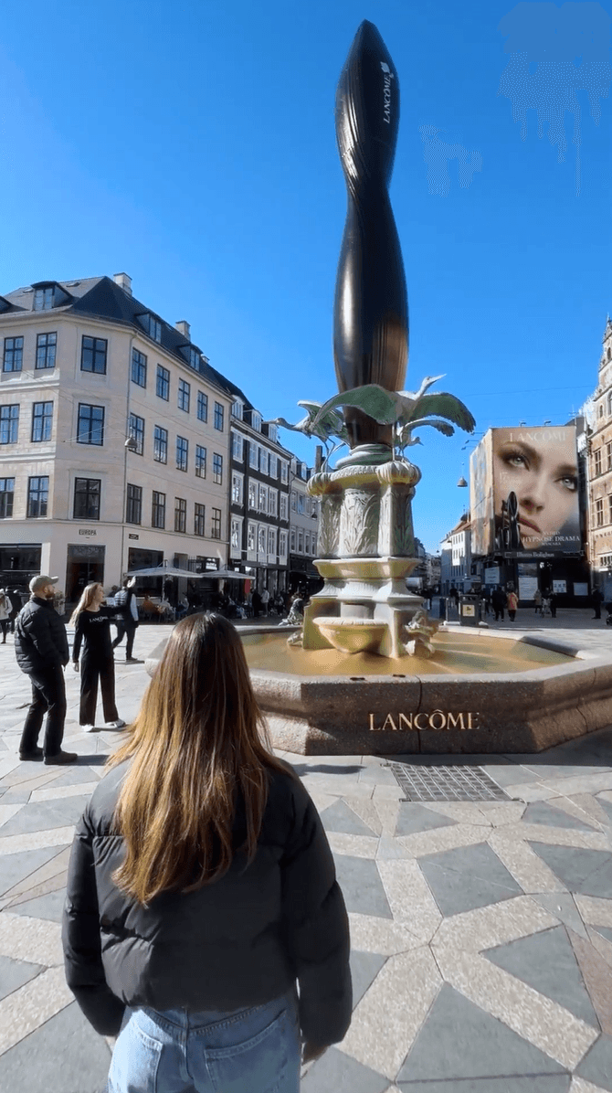 A woman looks at a Lancôme-branded city fountain featuring a giant mascara wand