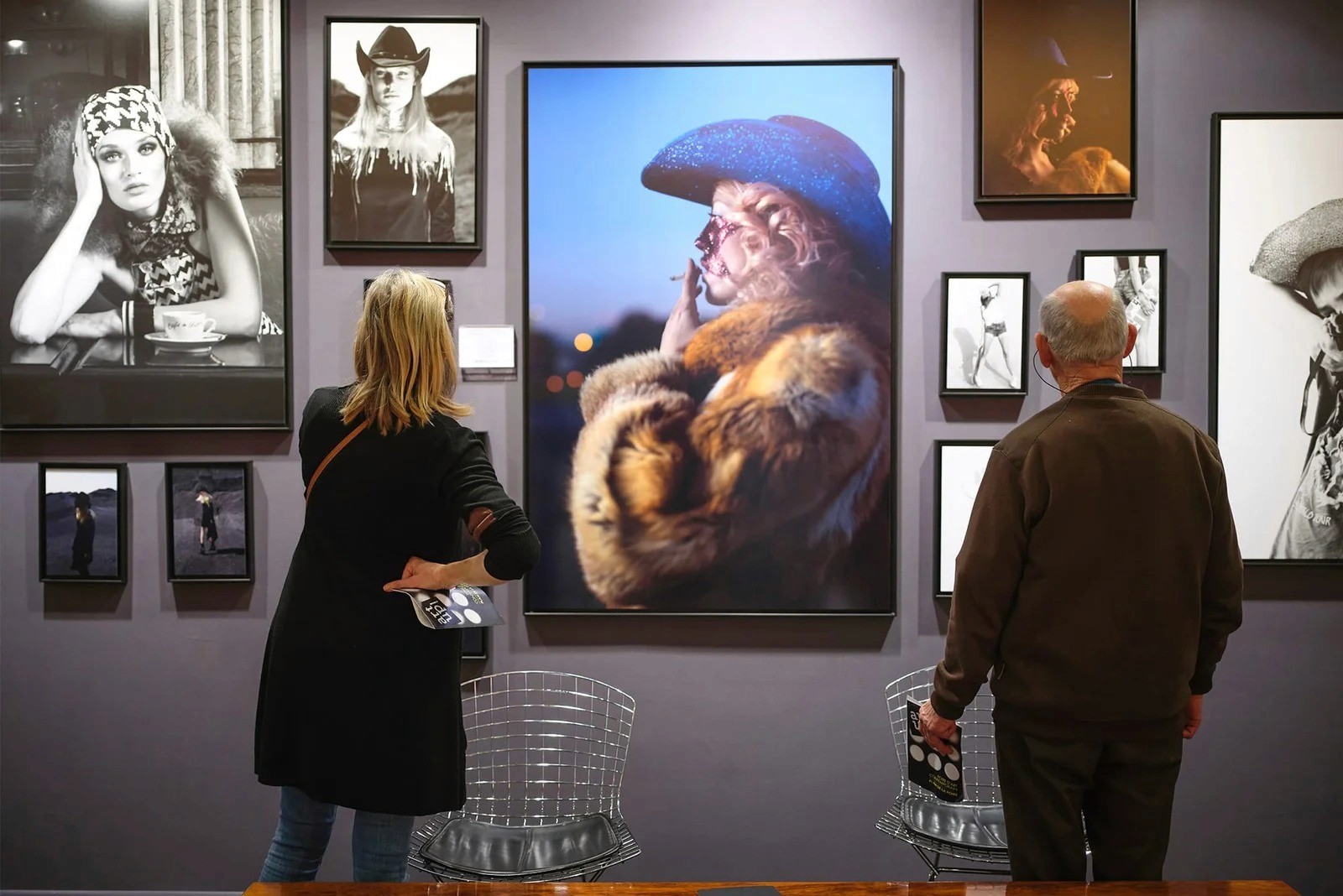 Deux personnes regardent des photographies encadrées. Exposition d'art avec portraits et images de femmes et d'hommes.