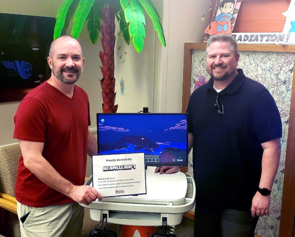 Hermitcraft creators Tango Tek and Impulse holding a Hermitcraft donor card in front of a new GO Kart that is being delivered to a children's hospital.