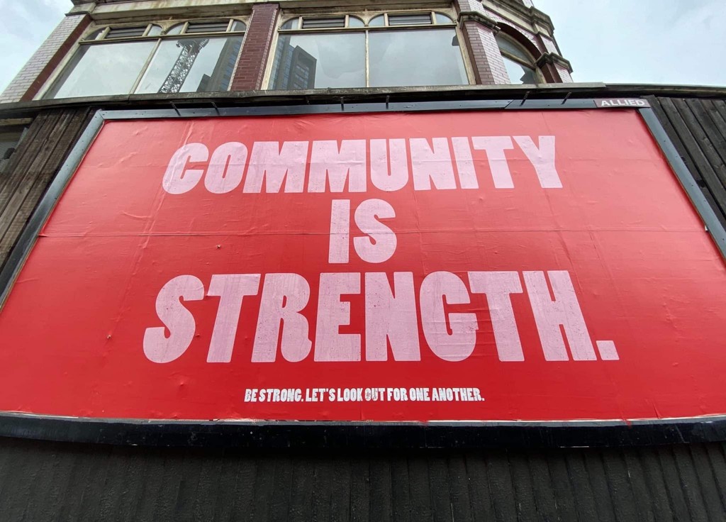 Red billboard with "Community is Strength" in bold white letters.