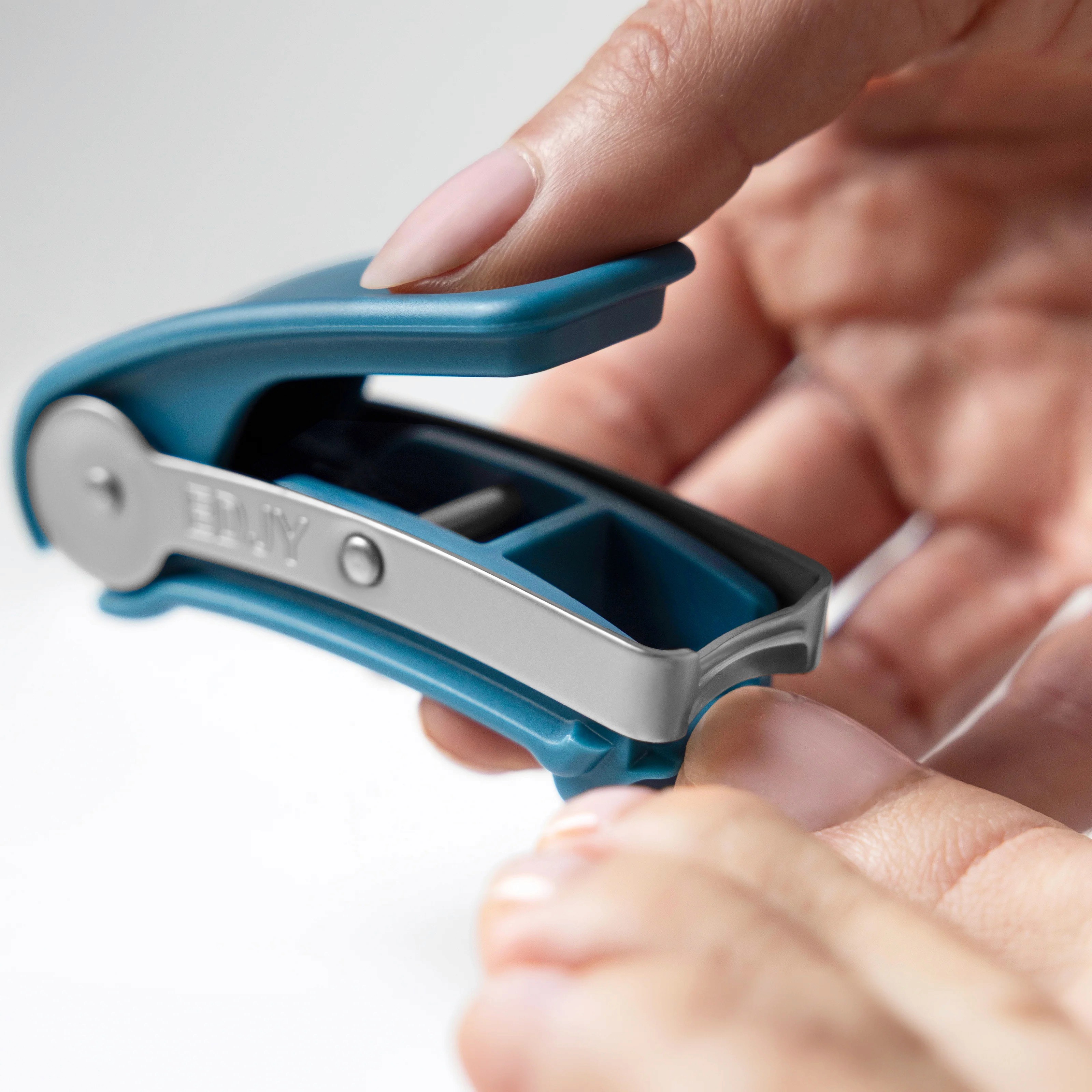 The EDJY toenail cutter in use, one hand squeezing the wide blue lever while the other guides the jaw to a nail.