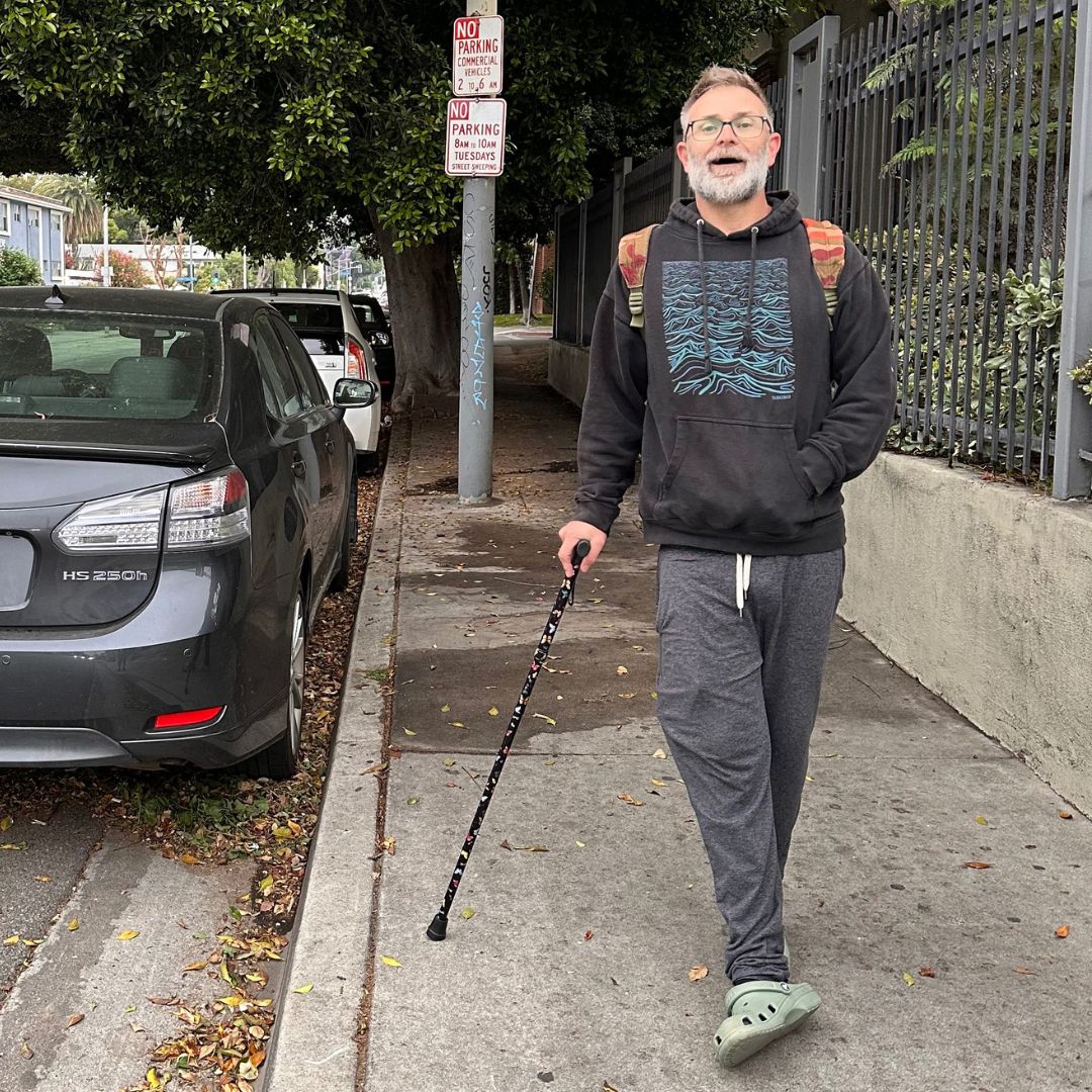 Picture of a man standing with a cane on the street by a gray car