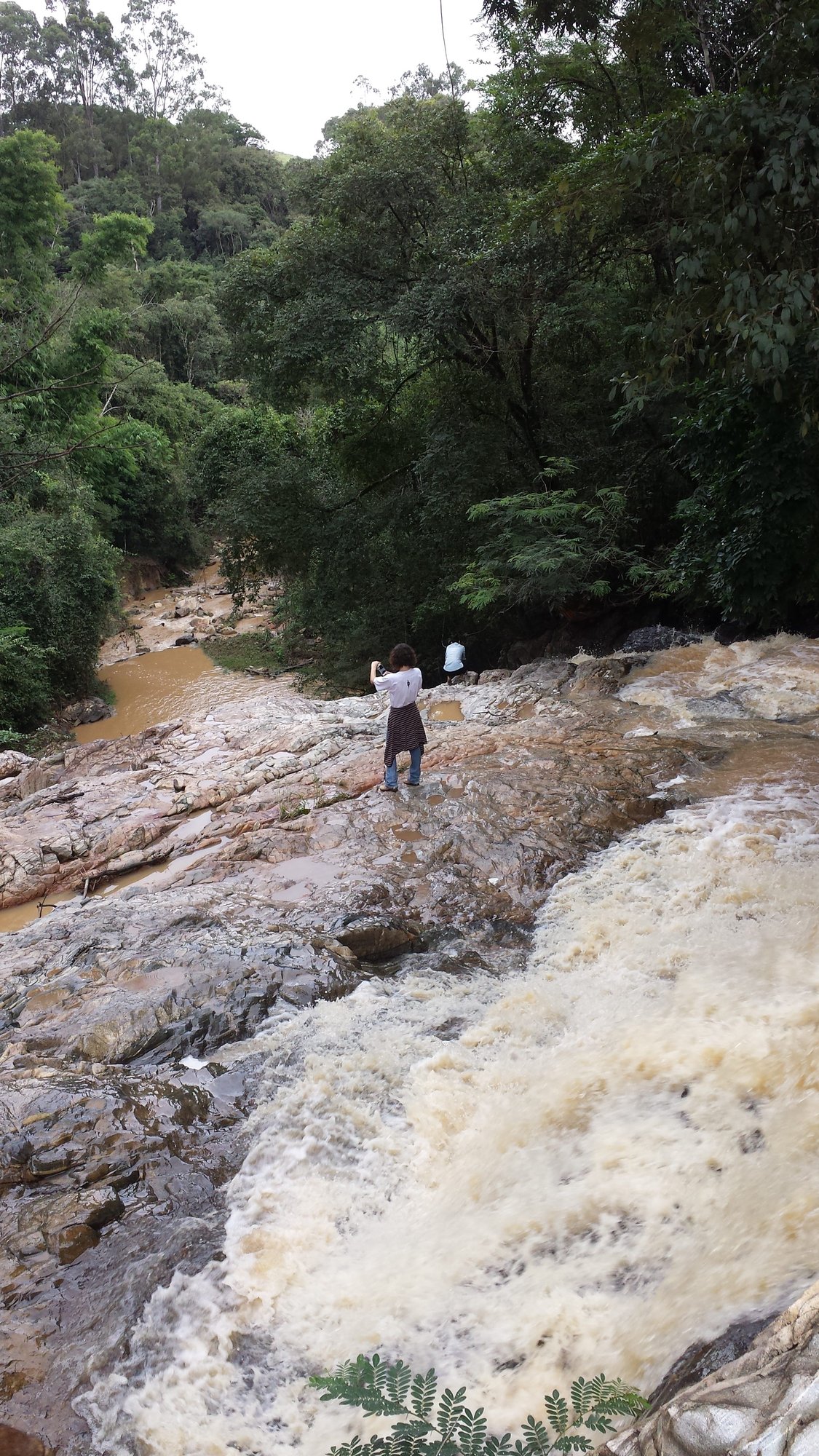 Pessoas sobre lajes de pedra junto a uma cachoeira na mata, durante o making of do projeto Vozes: Mulher