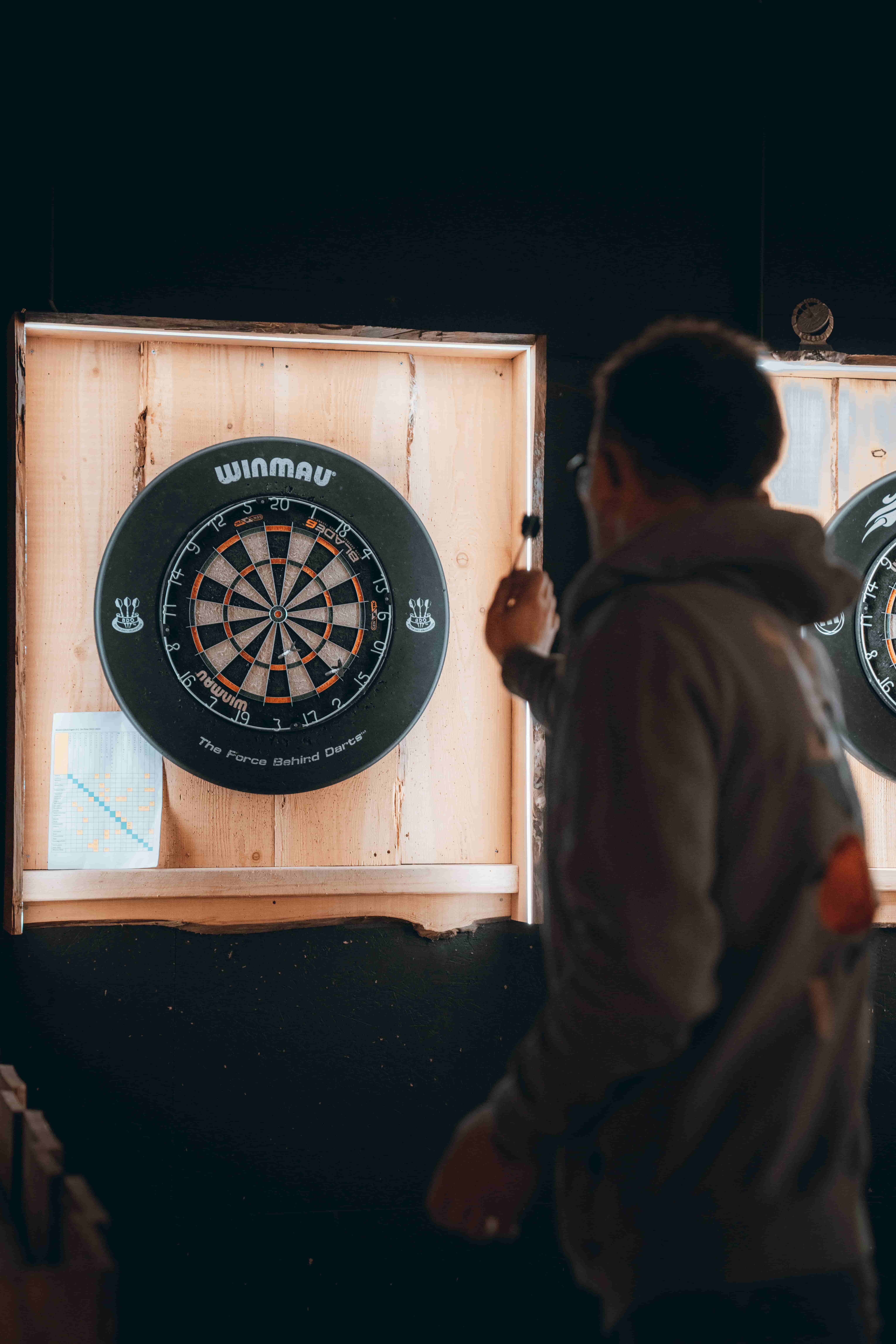 A man stands in front of a dartboard, preparing to throw a dart.