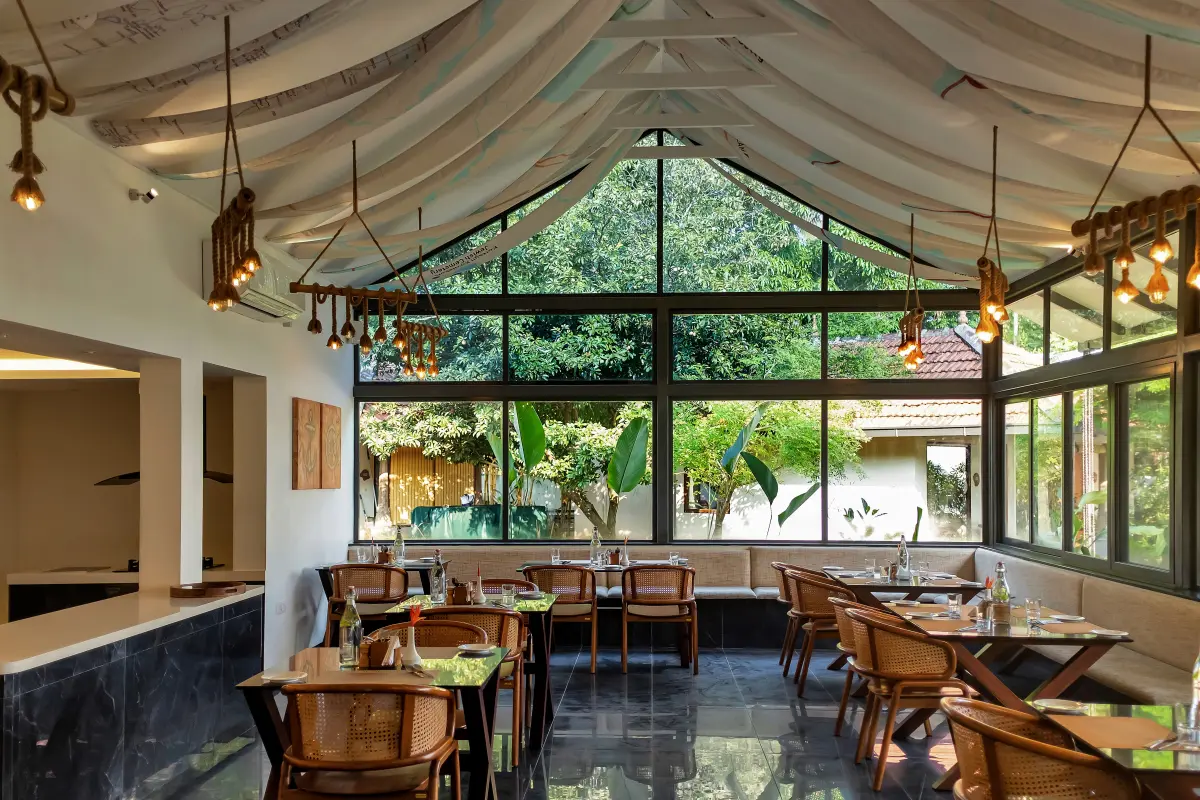 Sarvam dining hall at Vedic Village Kodungallur with a draped tent ceiling and floor-to-ceiling windows overlooking the garden, set for the Grand Traditional Sadhya