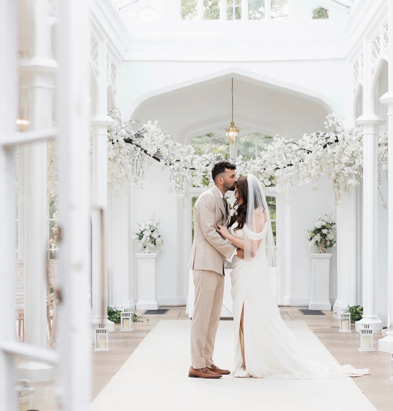 Newlyweds kissing beneath white wedding flowers