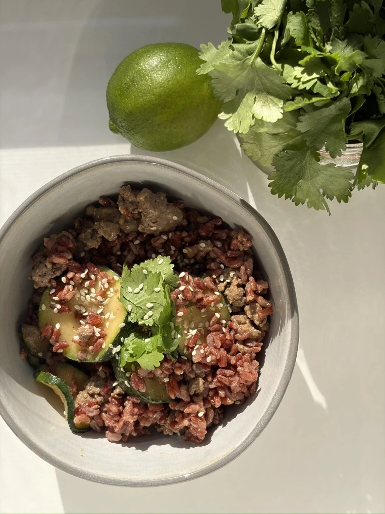 A stir-fried mix of sliced zucchini and browned beef coated in sesame dressing, finished with chopped fresh cilantro and sesame seeds.