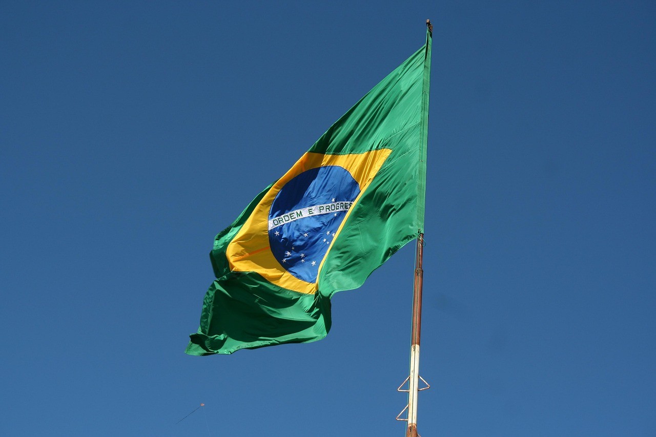 A flag of Brazil flies against a blue sky backdrop, representing the path to residency in Brazil through the investment visa.