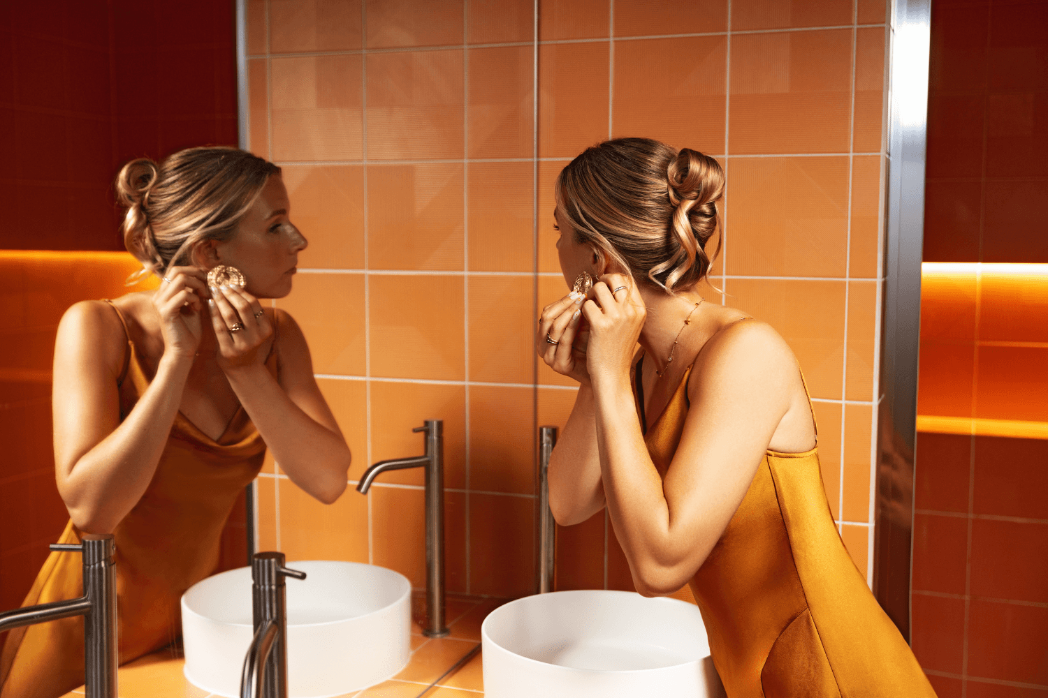 Woman looking in the mirror while getting ready, showing glowing skin from a professional spray tan