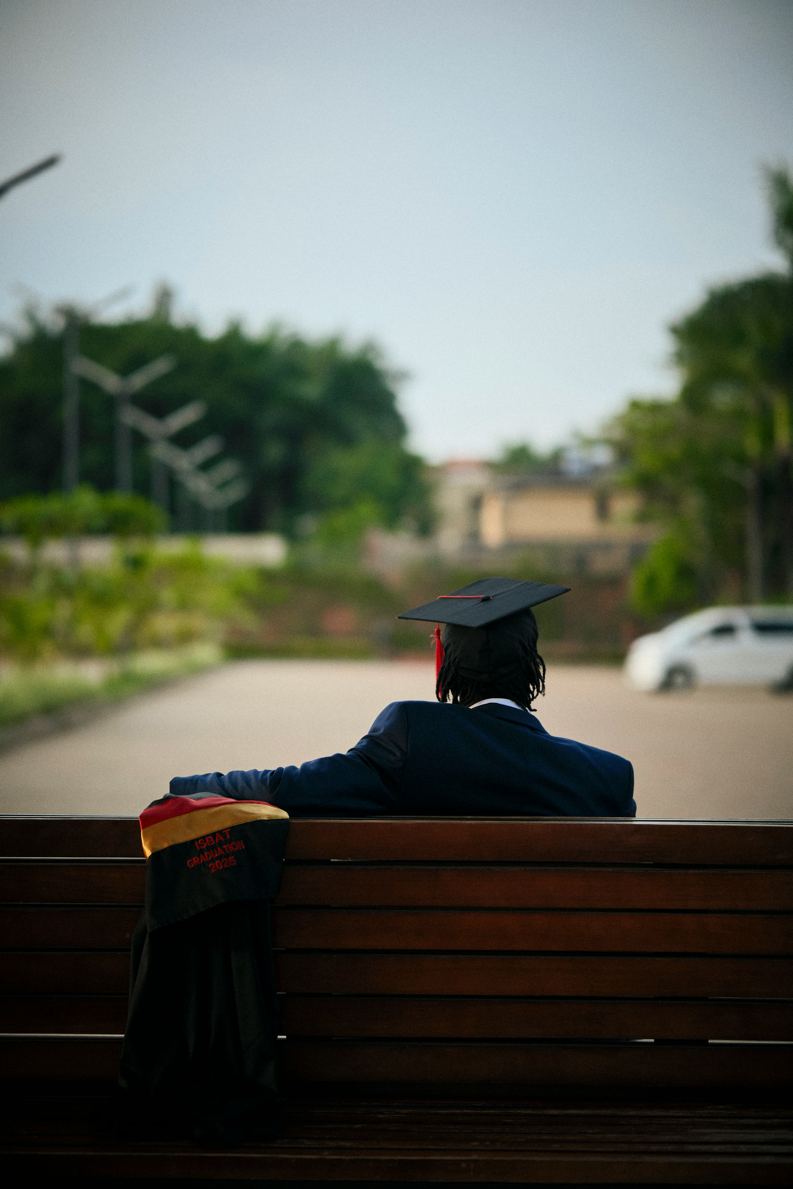 Graduate in cap and gown sits on a bench