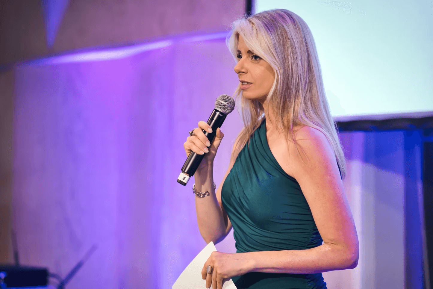 Blonde Moderatorin Désirée Lehmann moderiert vor blauem Hintergrun und hat ein Mikrophon in der Hand.