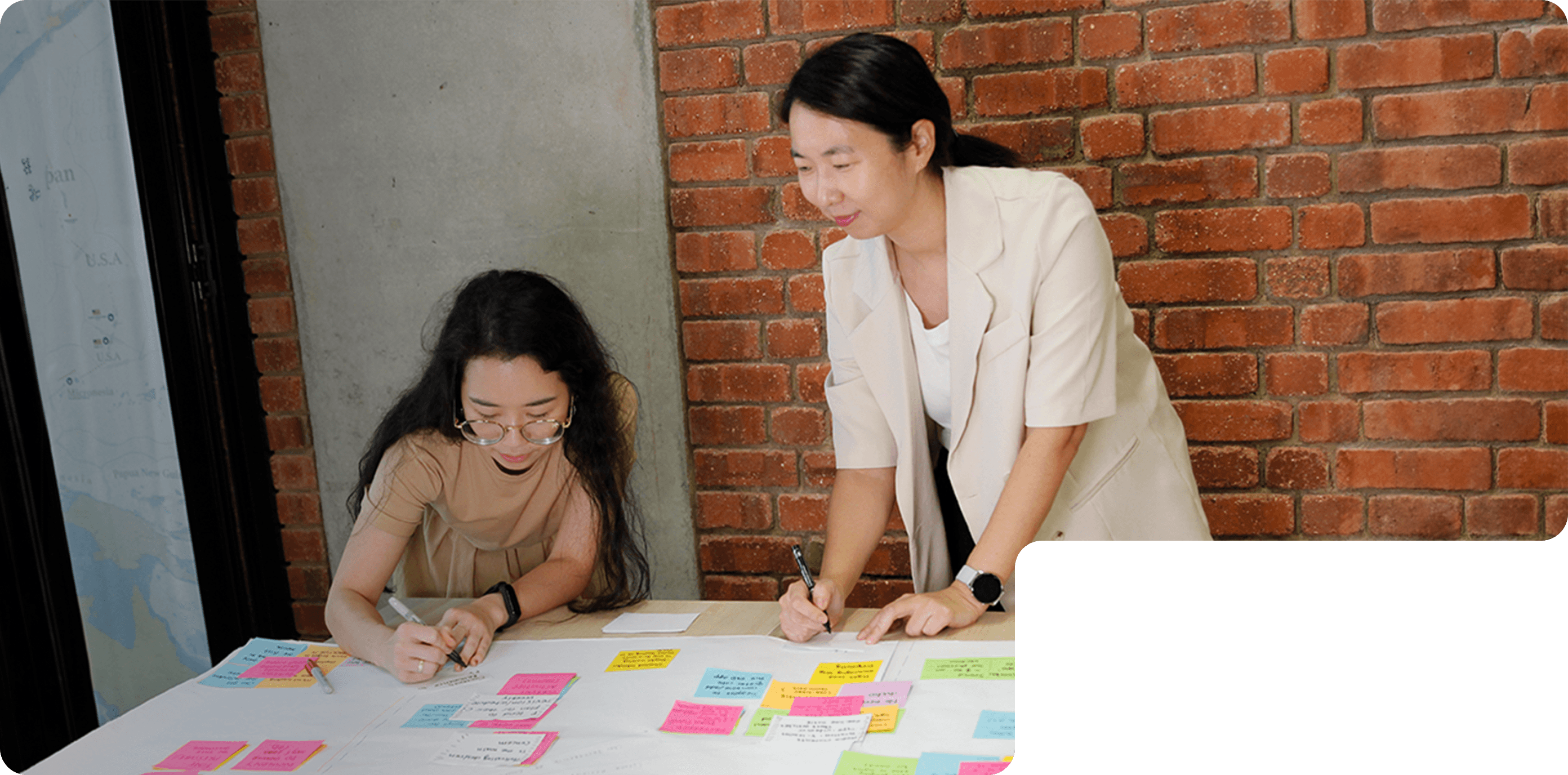 Two members of 55 Minutes collaborating at a table, writing on a large sheet filled with colorful sticky notes.