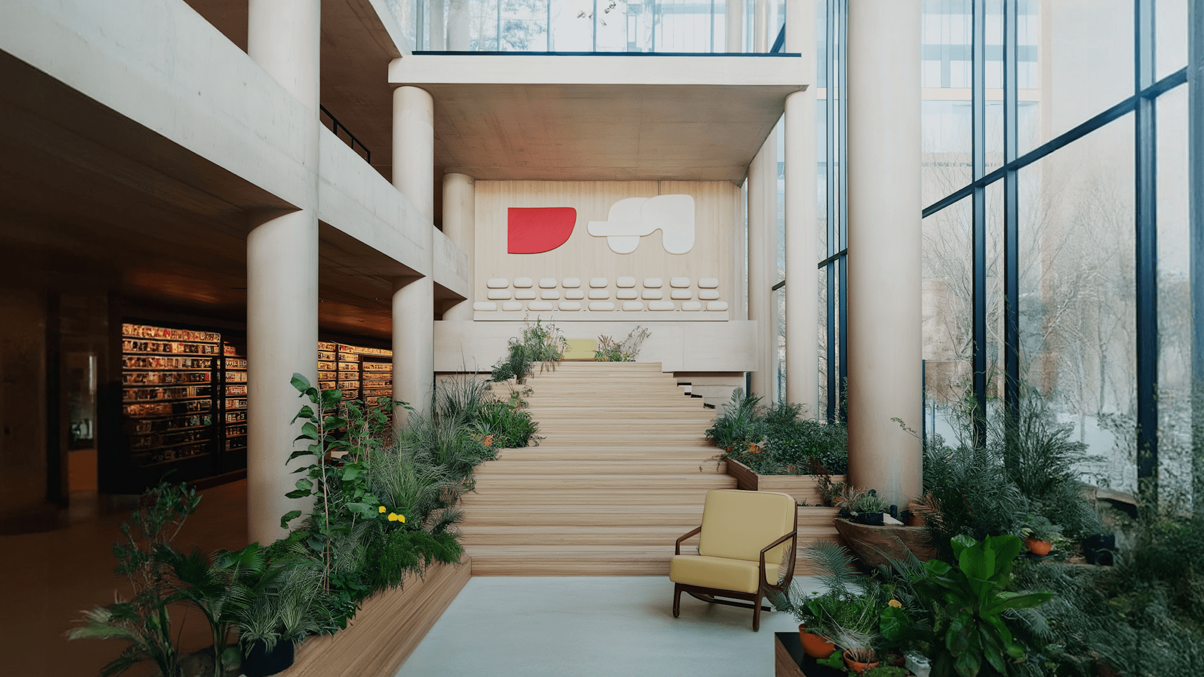 A pathway lined with plants, bordered by modern architecture, leading to an open area.