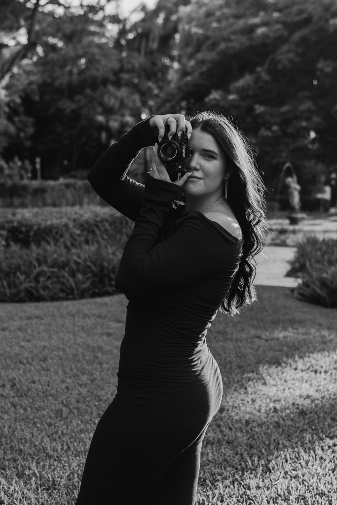     South Florida wedding photographer Makaela Skinner holding a film camera in a black and white self portrait outdoors.