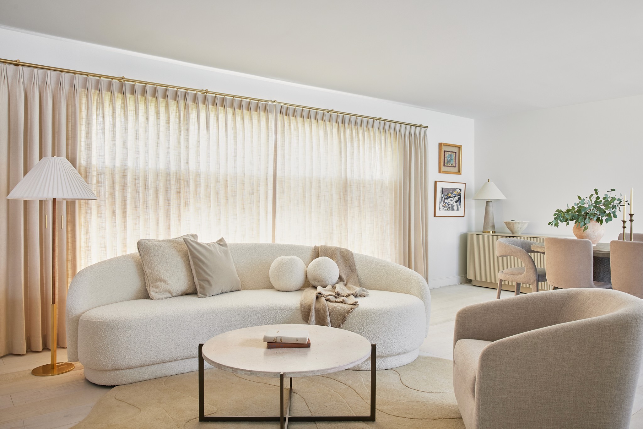 Beige living room with modern boucle sofa, round coffee table, a unique shaped rug, and window treatments by Jubilee Interiors in Los Angeles, California