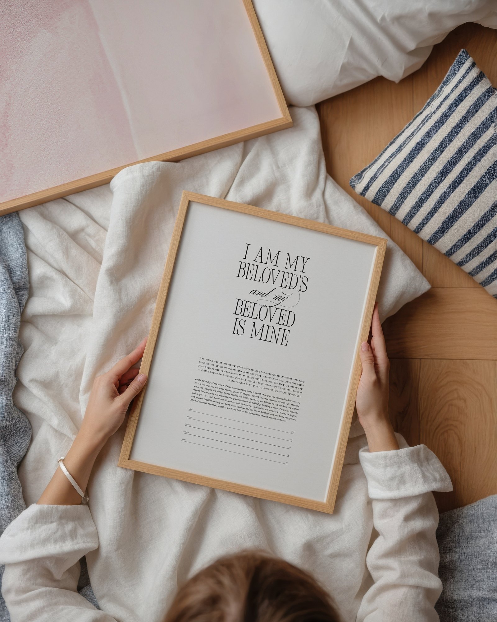 A woman lying on a bed holding the framed Bold & Beloved Ketubah