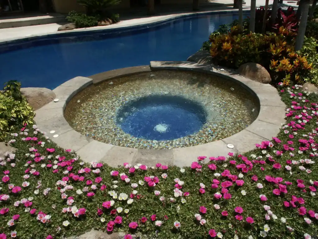 Round spa finished in a blue-green glass blend, set in a planted bed — Mosaiclegs Art Studio