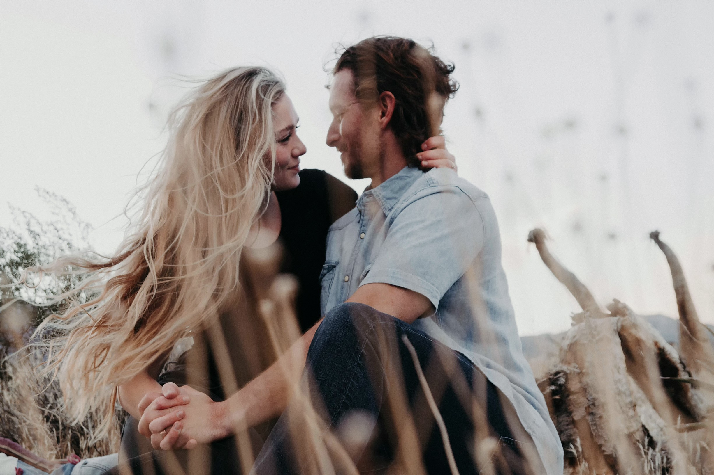 A couple sits closely on a rocky landscape with long grasses.