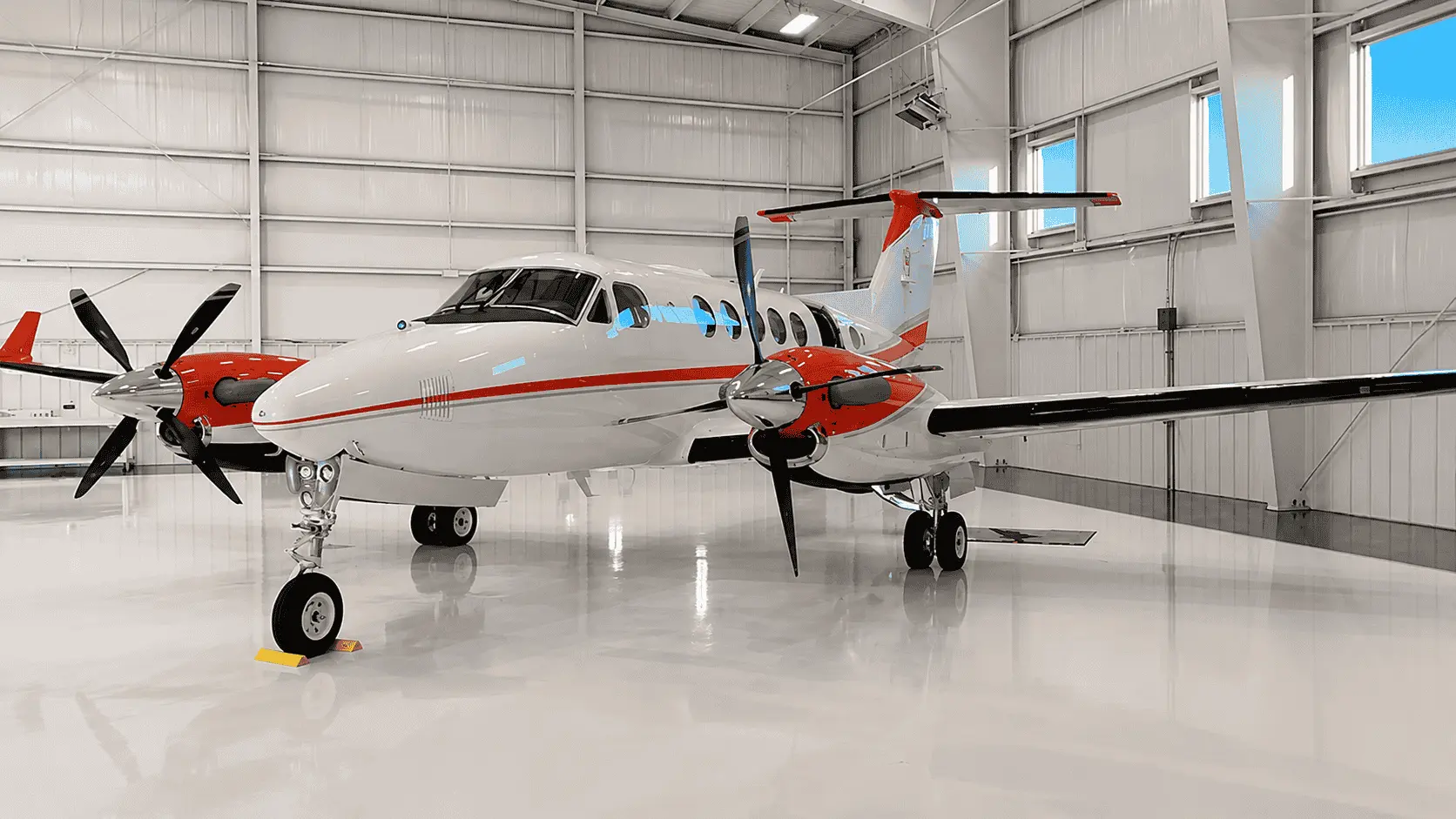 Twin-turboprop survey aircraft with red and white livery carrying Overwatch Imaging equipment, parked in a hangar
