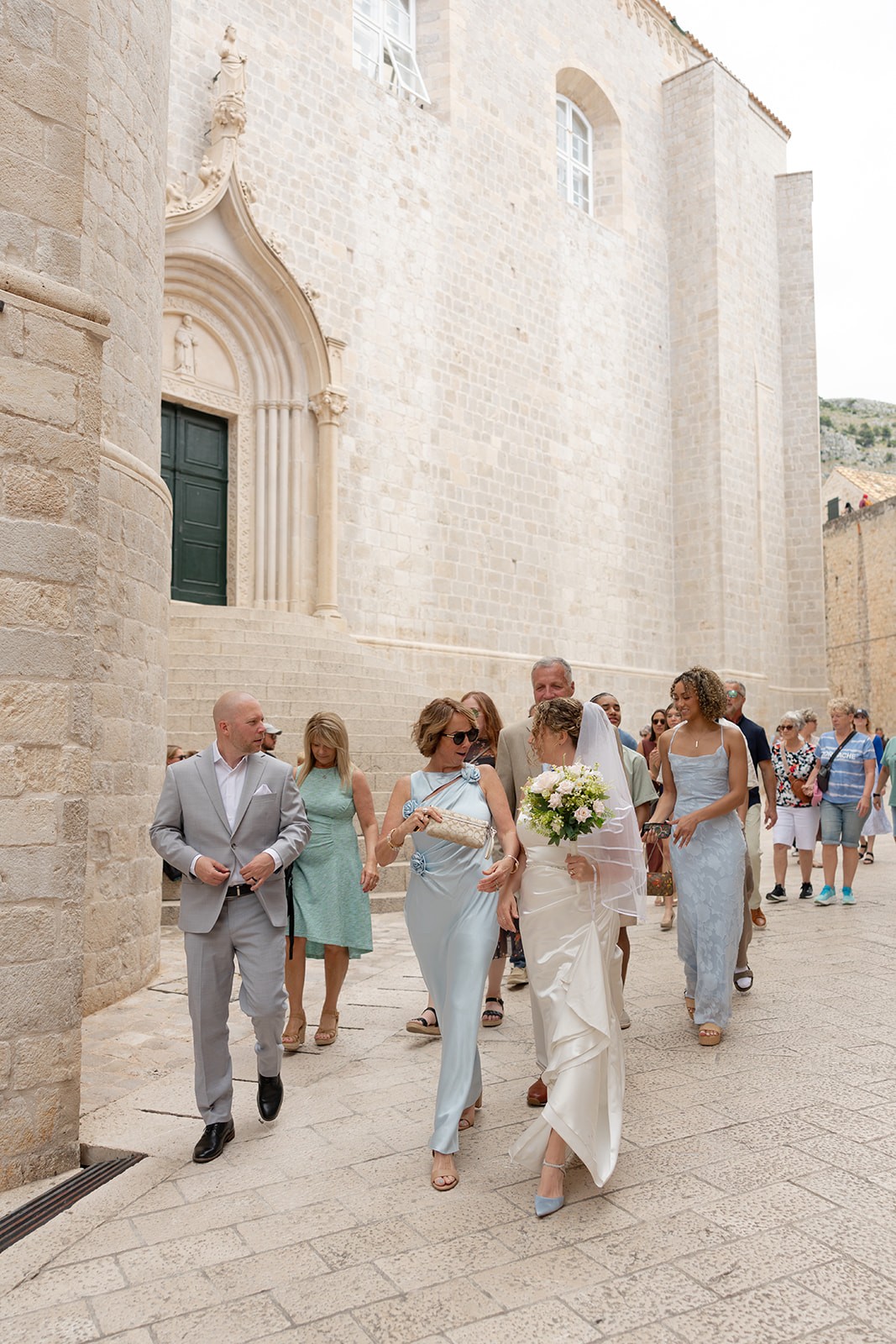 Bride and groom walking down the streets of Dubrovnik with their wedding party outside an old stone church in old town