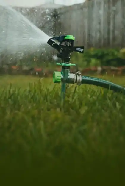Detalle de un sistema de riego por aspersión automático en pleno funcionamiento sobre el césped verde del jardín.