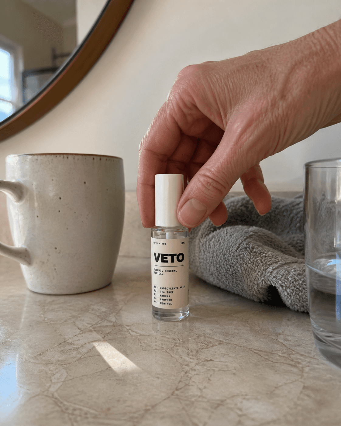 Hand holding a VETO bottle on a marble countertop with a mug and glass in the background.