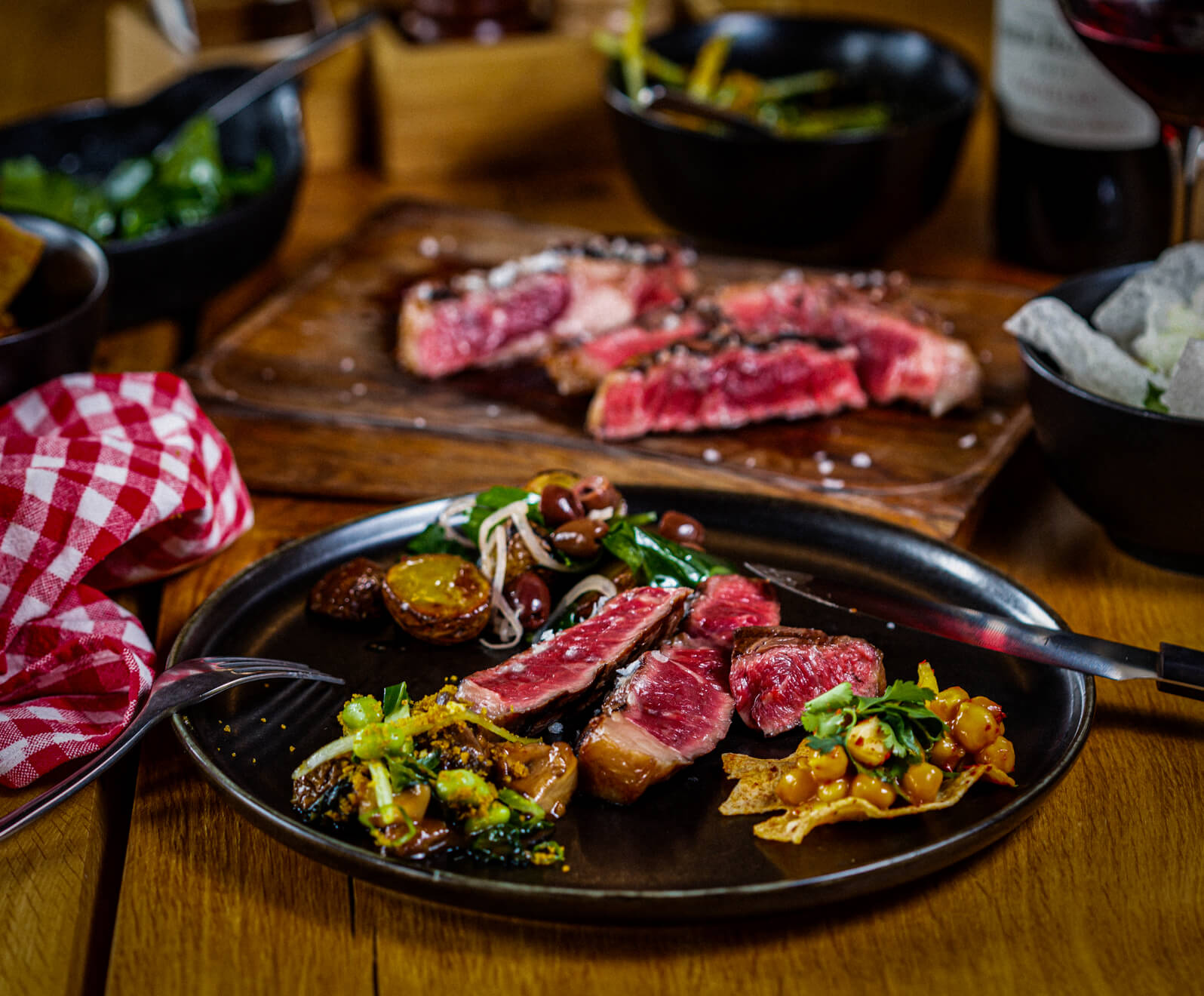Šťavnatý grilovaný steak servírovaný s hranolkami, zeleninou a červeným vínem v moderní restauraci.