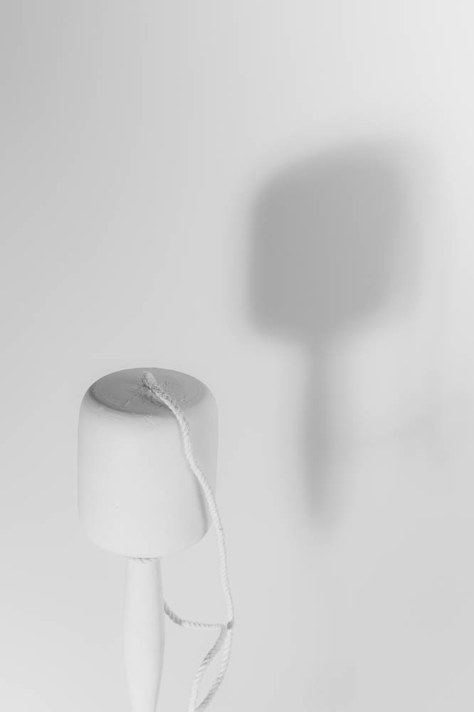 A wooden balero stands upright with its string loosely draped, casting a soft shadow that mirrors its shape in silence.