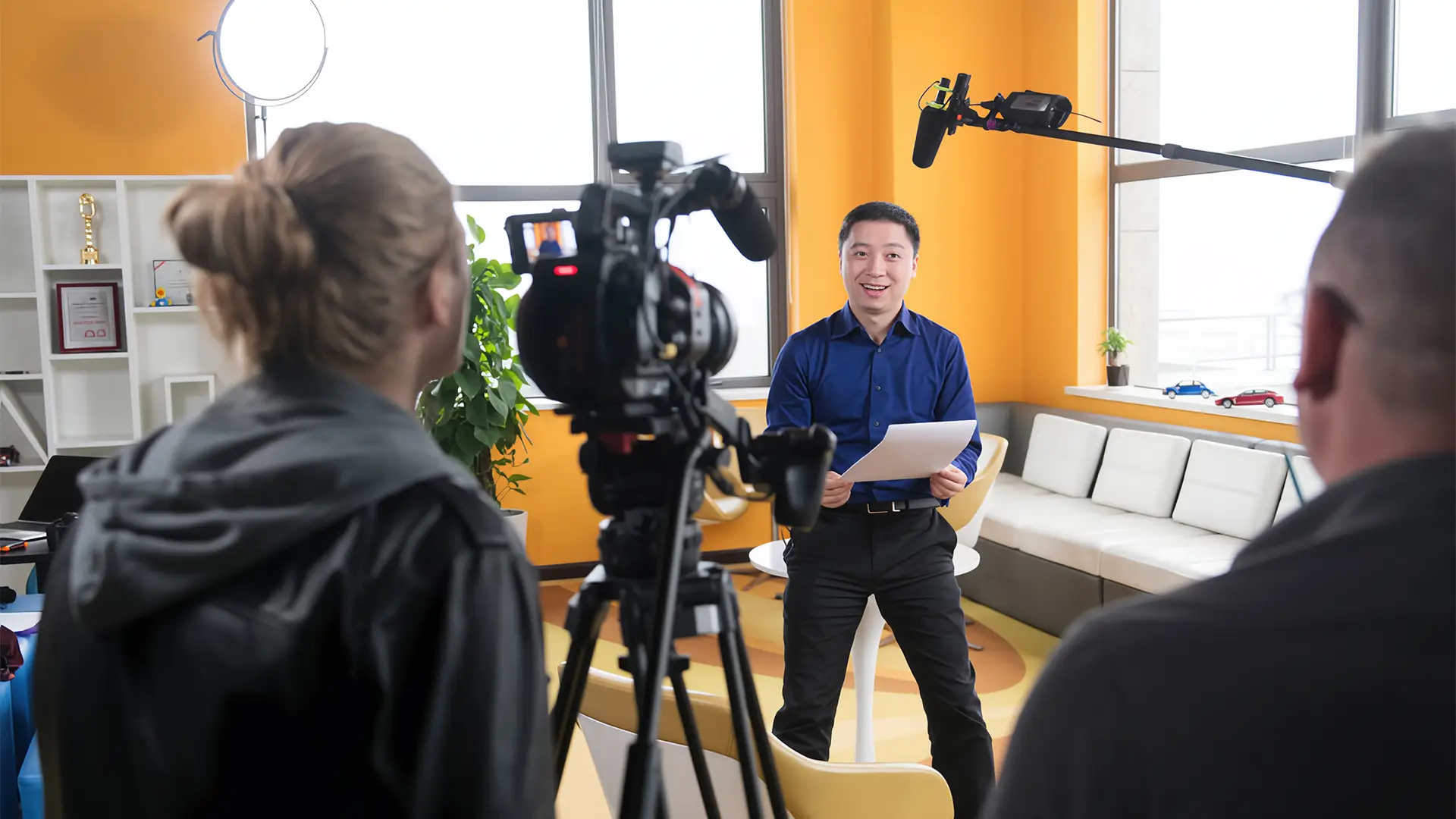 Camera operator filming a Cox Automotive colleague reading from notes in a modern office setting.