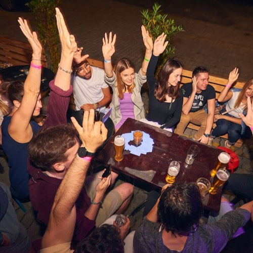 A group of pub crawl participants raising hands around a table with beers on it