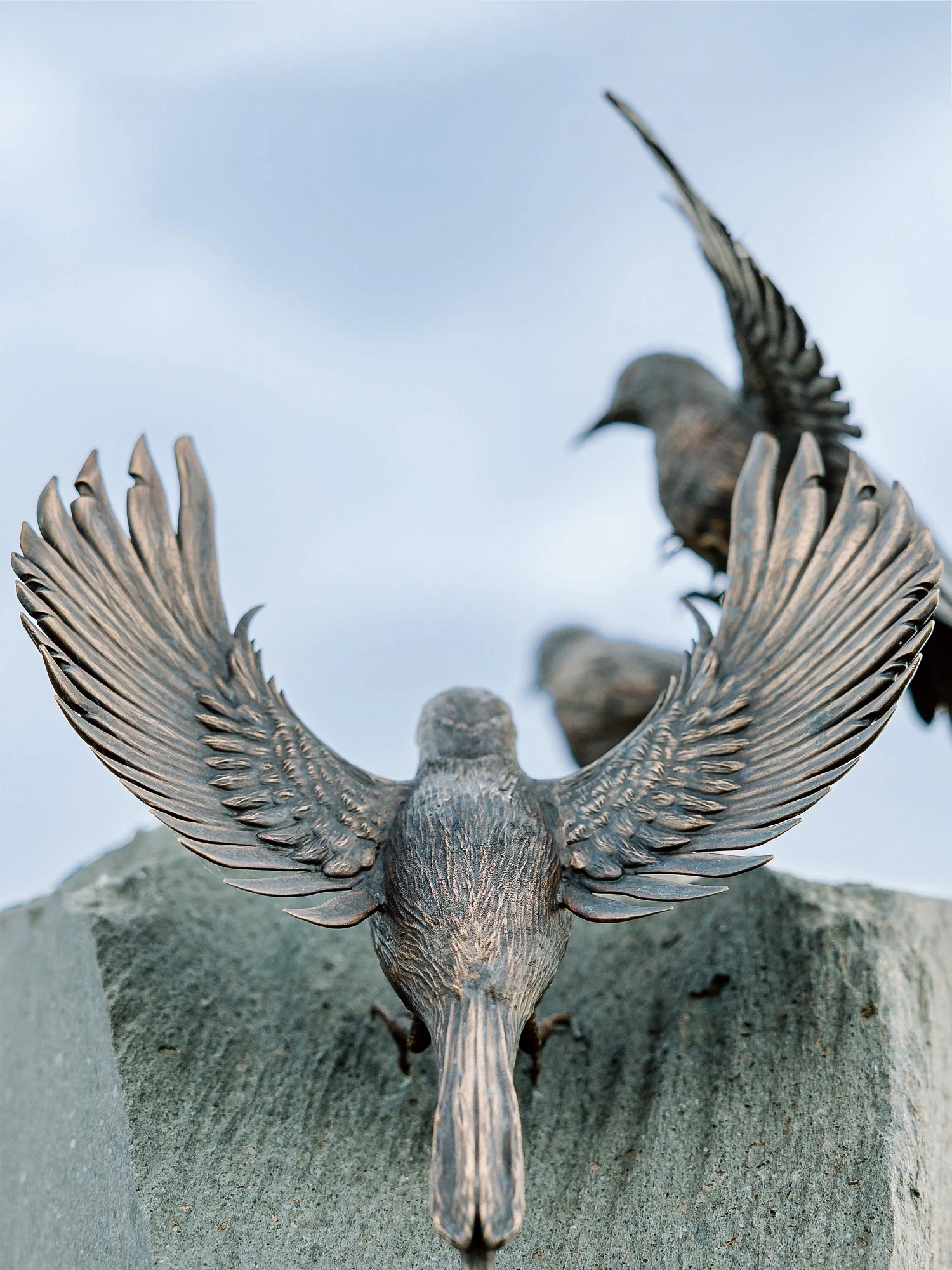 Close-up of sculpted bronze birds taking flight atop a custom slate stone monument created by artist Shaun Leane.