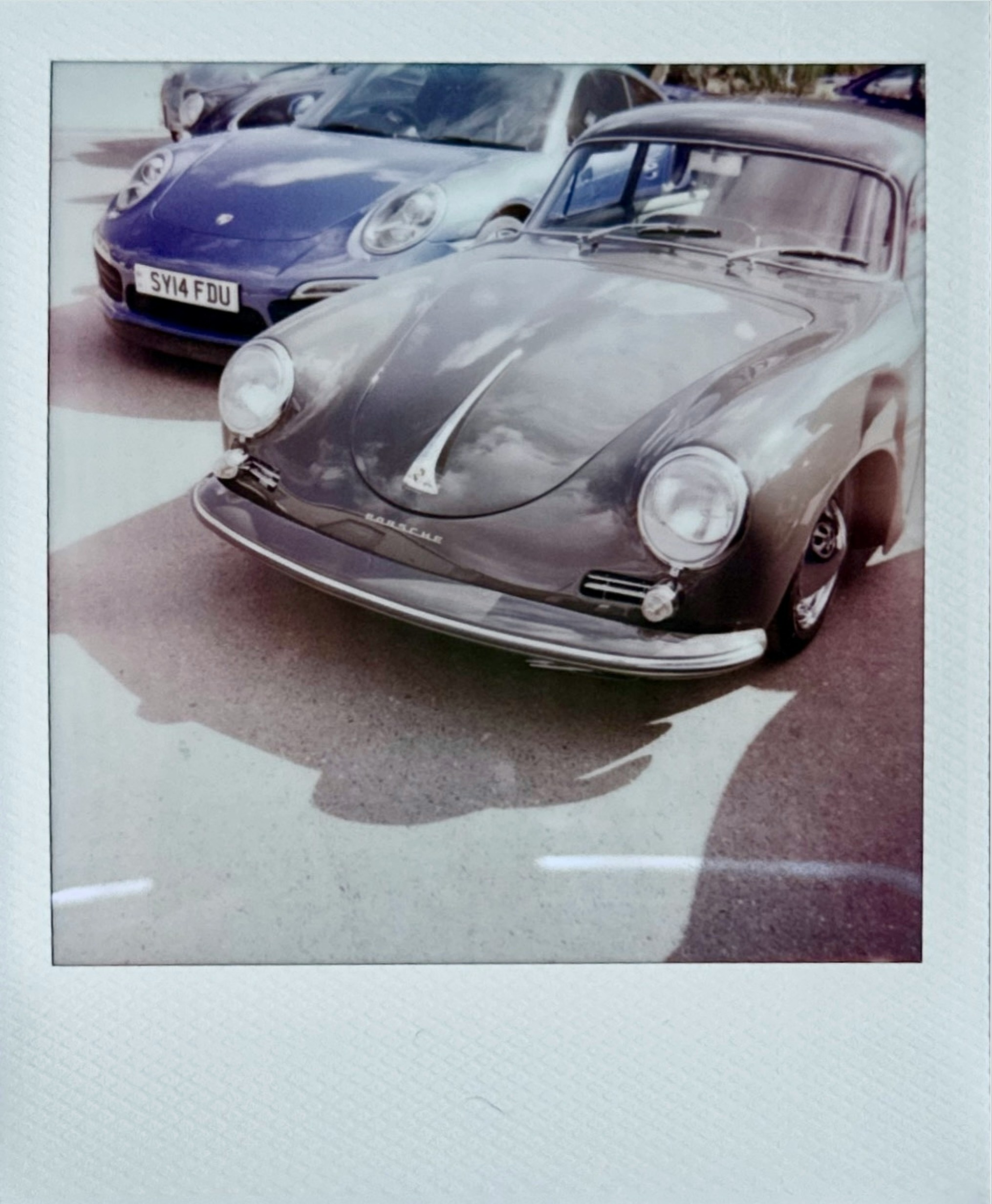 Classic grey porsche parked next to a blue porsche.