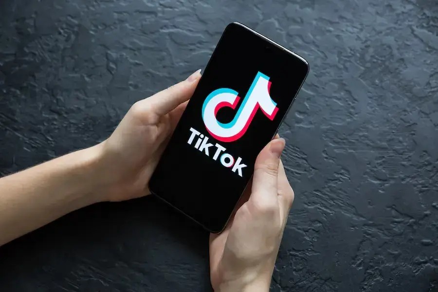 A person holding a phone with the TikTok logo shown towards the viewer, symbolising them opening up the social media platform.
