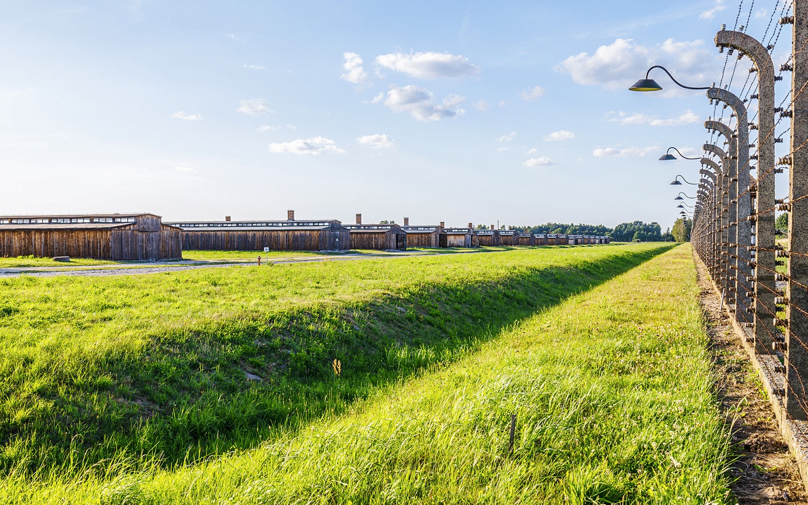 Baracker och taggtrådsstängsel i Auschwitz II under en klar himmel.