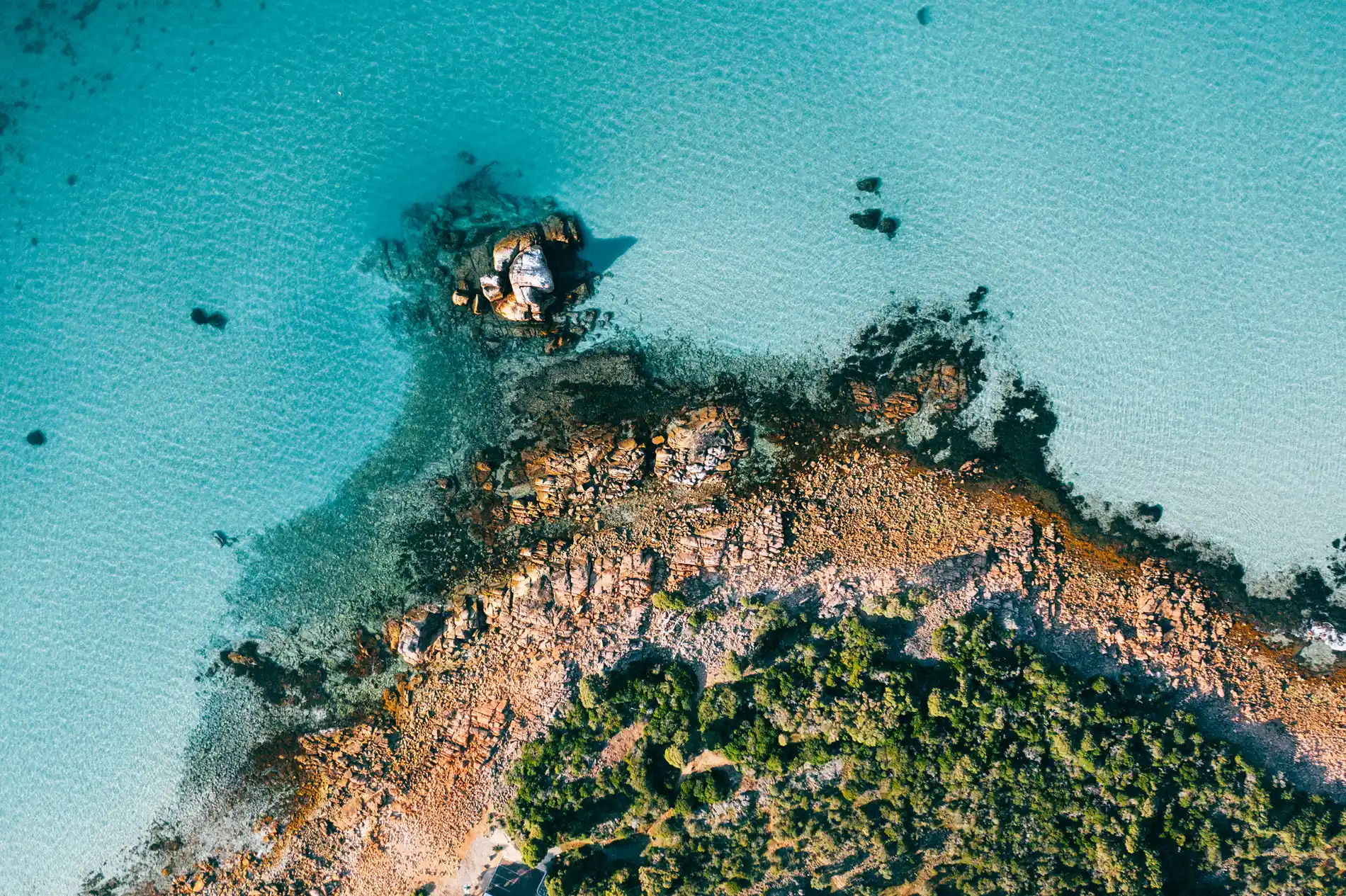 Aerial of a low rocky headland surrounded by bright turquoise shallows