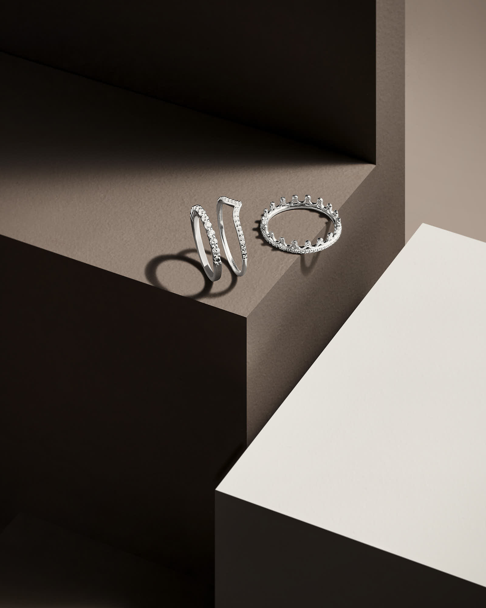 Three metallic rings are resting at the edge of a minimalist geometric setup featuring dark and light surfaces.