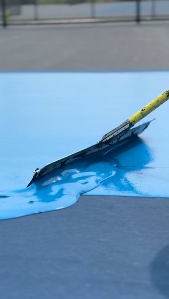 Close up of a squeegee spreading wet blue coating on a court