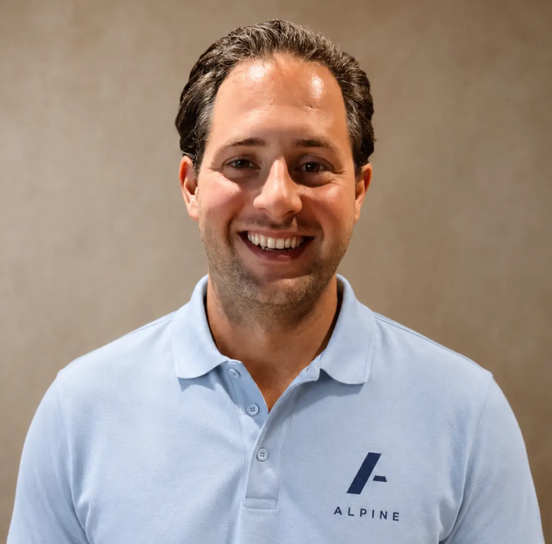 Professional headshot of a man with short brown hair and a light beard. He wears a navy blazer and gray shirt, conveying confidence and approachability.