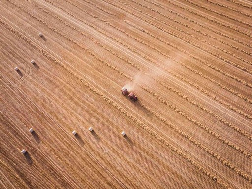 Aerial view of a tractor harvesting a wheat field, with rows of straw and hay bales representing the agricultural waste used in Strawtown's compressed straw building panels