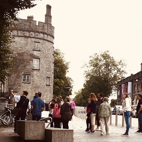 一群人站在一座历史悠久的石塔附近，背景是一些树木和几个混凝土障碍。