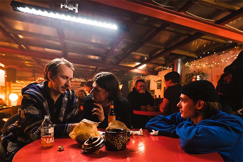 Director Meel Paliale guides actors Mihkel Kuusk (Sebastian) and Karl Birnbaum (Silo) as they sit in a bar during the filming of Pikad paberid (Rolling Papers)